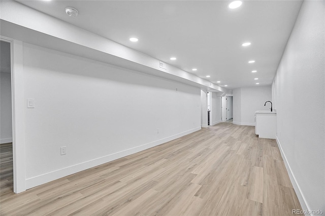 basement featuring recessed lighting, baseboards, a sink, and light wood finished floors