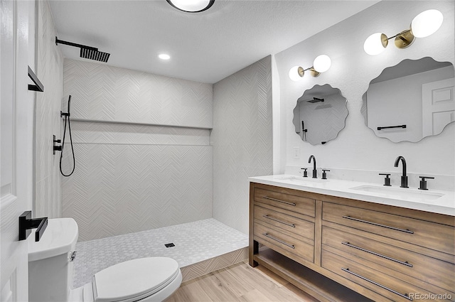 bathroom with a tile shower, a textured ceiling, toilet, vanity, and hardwood / wood-style flooring