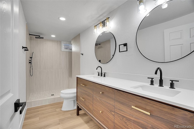 bathroom featuring toilet, hardwood / wood-style floors, vanity, and a tile shower