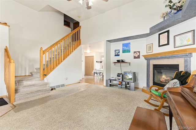 living room featuring a towering ceiling, a fireplace, ceiling fan, and carpet flooring