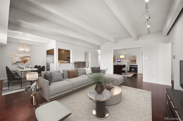 living room with dark wood-type flooring, rail lighting, an inviting chandelier, a textured ceiling, and beamed ceiling