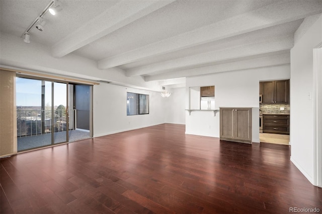 unfurnished living room with rail lighting, dark hardwood / wood-style flooring, beam ceiling, and a textured ceiling