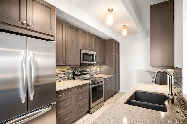 kitchen featuring stainless steel appliances, hanging light fixtures, sink, and light stone counters