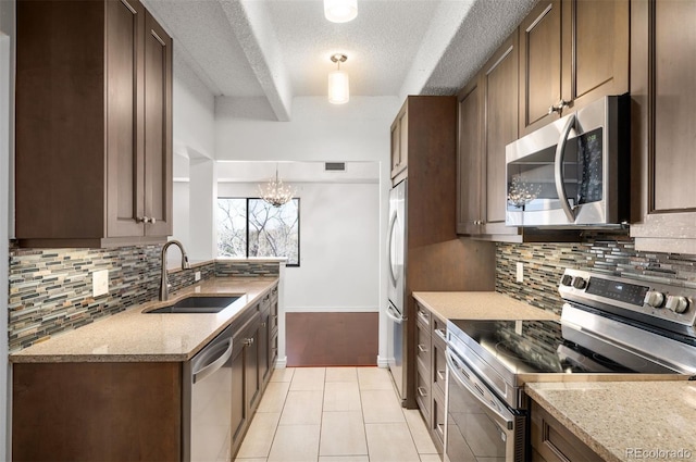 kitchen with appliances with stainless steel finishes, pendant lighting, sink, decorative backsplash, and light stone counters