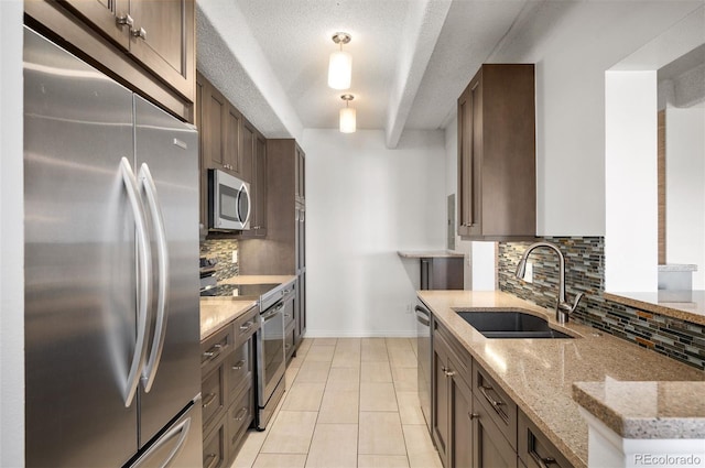 kitchen with tasteful backsplash, sink, hanging light fixtures, stainless steel appliances, and light stone countertops