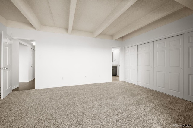 unfurnished bedroom with a closet, beam ceiling, carpet, and a textured ceiling