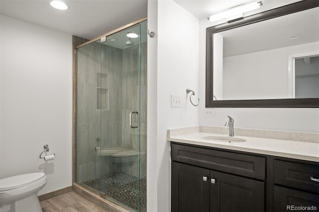 bathroom with hardwood / wood-style flooring, vanity, a shower with shower door, and toilet