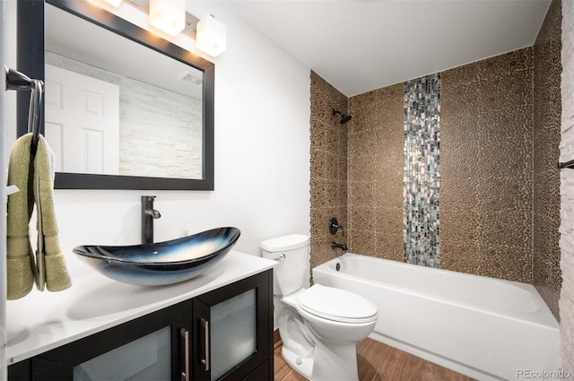 full bathroom featuring hardwood / wood-style flooring, tiled shower / bath, vanity, and toilet