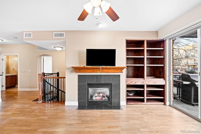 living room featuring ceiling fan, a tile fireplace, and light hardwood / wood-style flooring