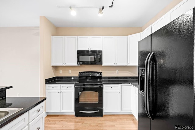 kitchen with dark stone countertops, white cabinetry, black appliances, and light wood-type flooring