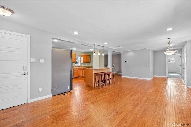 kitchen with light hardwood / wood-style floors, light stone countertops, pendant lighting, a breakfast bar, and stainless steel refrigerator