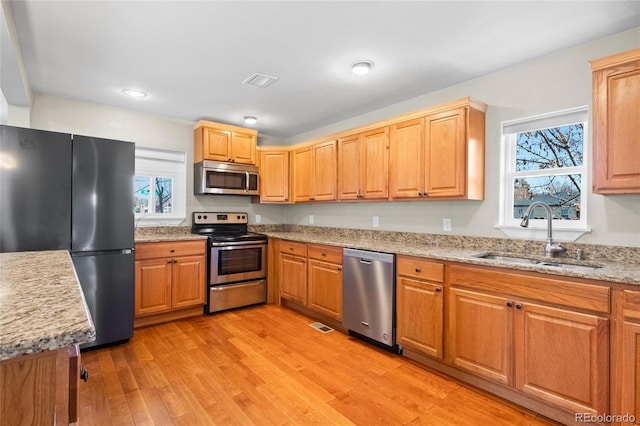 kitchen with light wood-type flooring, appliances with stainless steel finishes, light stone counters, and sink