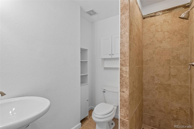 bathroom with sink, toilet, a tile shower, and tile patterned flooring