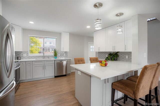 kitchen with pendant lighting, kitchen peninsula, a breakfast bar area, white cabinetry, and stainless steel appliances