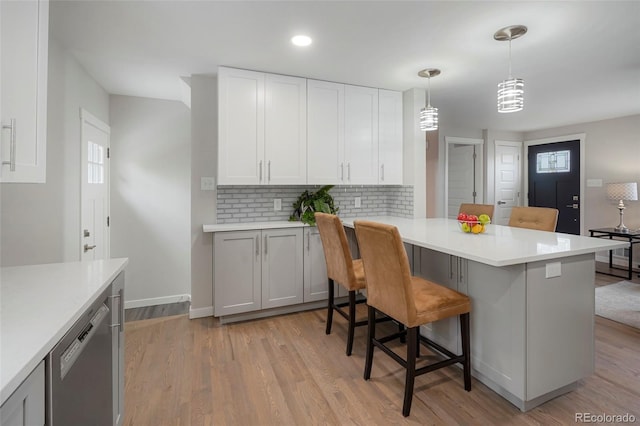 kitchen featuring kitchen peninsula, white cabinets, dishwasher, hanging light fixtures, and a breakfast bar area