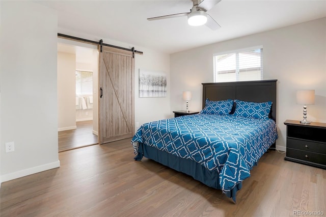 bedroom featuring ceiling fan, a barn door, wood-type flooring, and connected bathroom