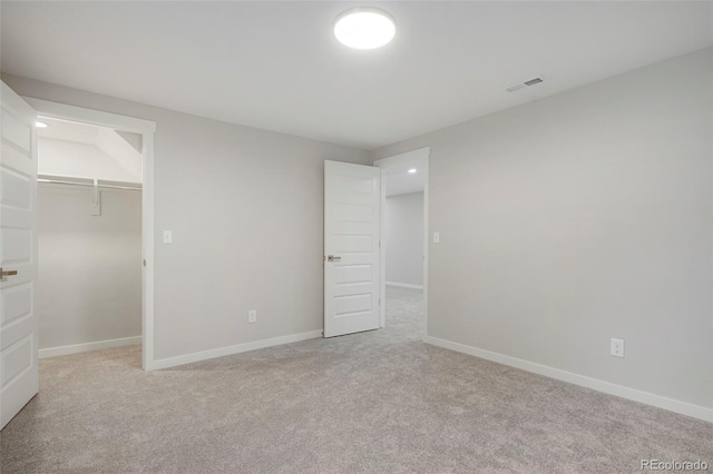 unfurnished bedroom featuring a spacious closet, a closet, and light colored carpet