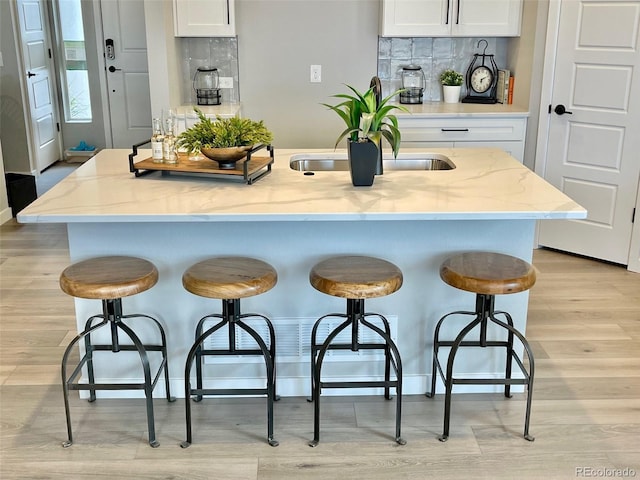 kitchen featuring a kitchen island with sink, light stone counters, a kitchen bar, decorative backsplash, and white cabinets