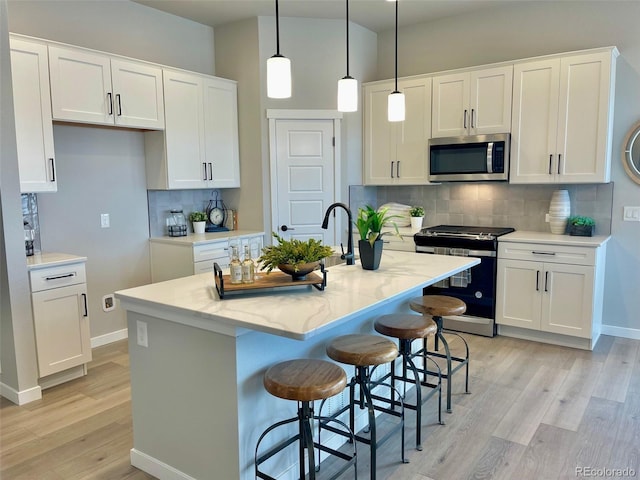 kitchen with appliances with stainless steel finishes, a center island with sink, white cabinetry, and pendant lighting