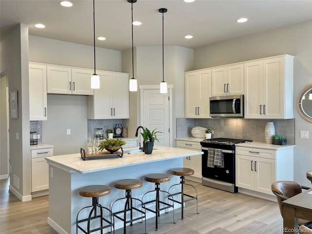 kitchen featuring a kitchen island with sink, white cabinets, pendant lighting, and appliances with stainless steel finishes
