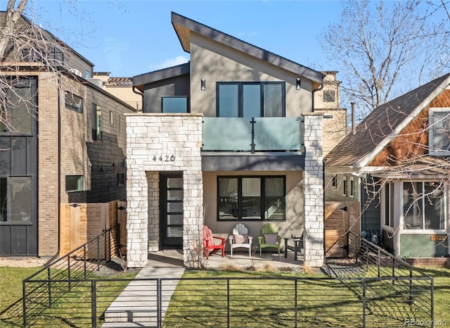 view of front facade featuring a front lawn, a balcony, a fenced front yard, and stucco siding