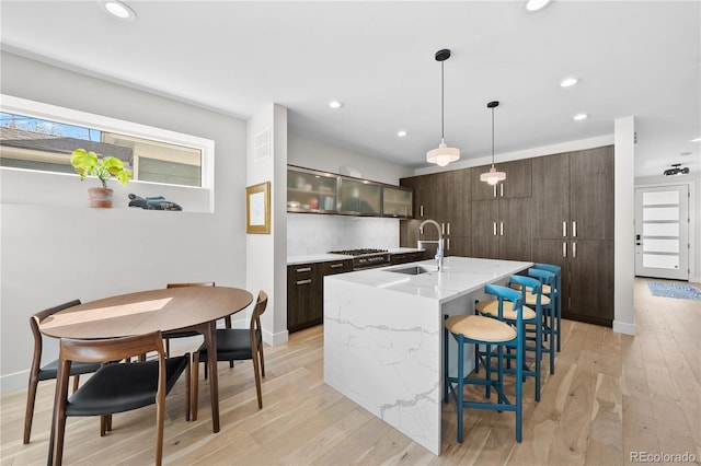 kitchen featuring light wood-type flooring, an island with sink, a sink, a kitchen breakfast bar, and backsplash