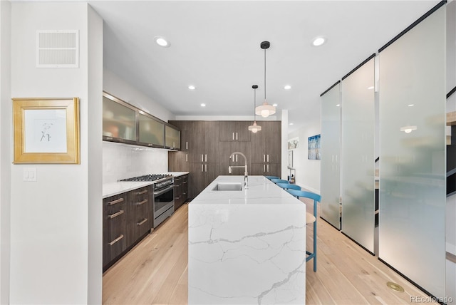 kitchen featuring high end range, modern cabinets, light wood-type flooring, and a sink