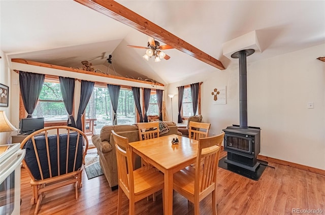 dining area with light wood finished floors, vaulted ceiling with beams, a wood stove, and a ceiling fan