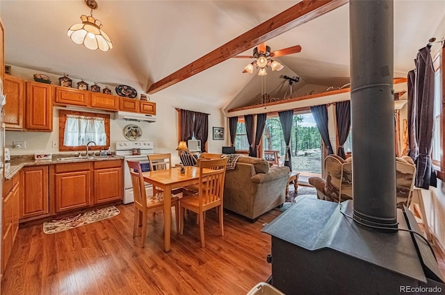 dining area with lofted ceiling with beams, a wood stove, light wood-style flooring, and ceiling fan