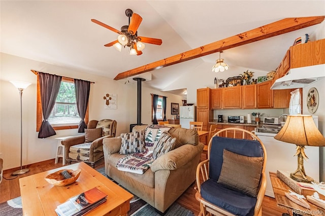 living area with vaulted ceiling, a ceiling fan, a wood stove, and wood finished floors
