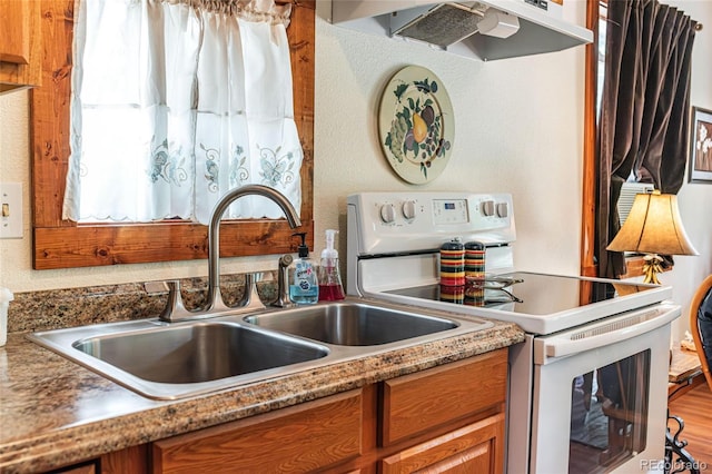 kitchen featuring brown cabinets, white electric range, under cabinet range hood, and a sink