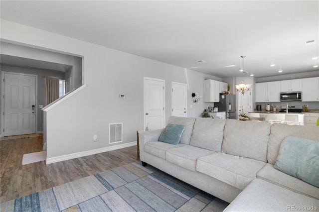 living room with visible vents, baseboards, a notable chandelier, and wood finished floors