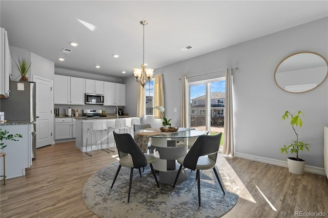 dining area with light wood-type flooring, visible vents, baseboards, and an inviting chandelier