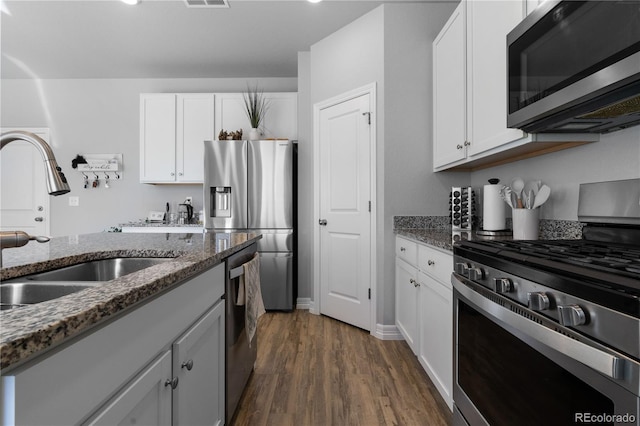 kitchen with dark wood-type flooring, a sink, dark stone countertops, white cabinetry, and appliances with stainless steel finishes