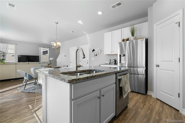 kitchen with visible vents, dark stone counters, a kitchen island with sink, a sink, and stainless steel appliances