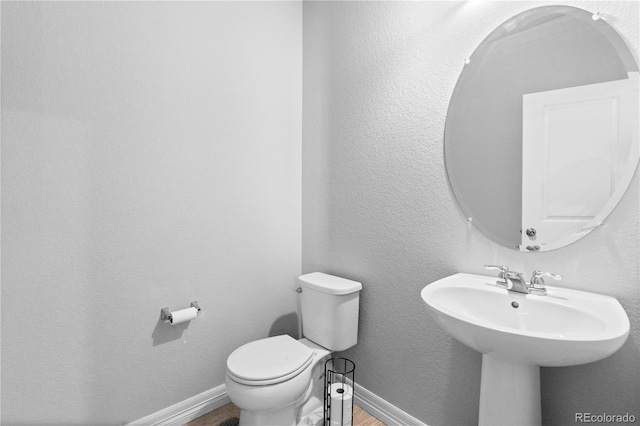 half bath featuring a textured wall, toilet, baseboards, and wood finished floors