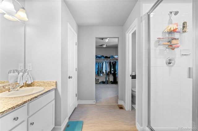 full bathroom with vanity, a spacious closet, a shower stall, and toilet