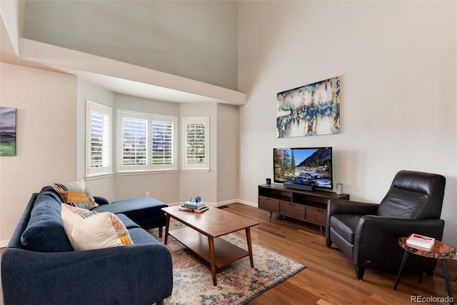 living room with wood finished floors, baseboards, and a high ceiling