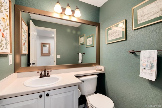 half bath featuring toilet, vanity, and a textured wall