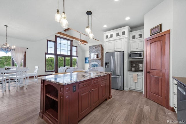 kitchen featuring appliances with stainless steel finishes, a kitchen island, decorative light fixtures, tasteful backsplash, and light wood-type flooring