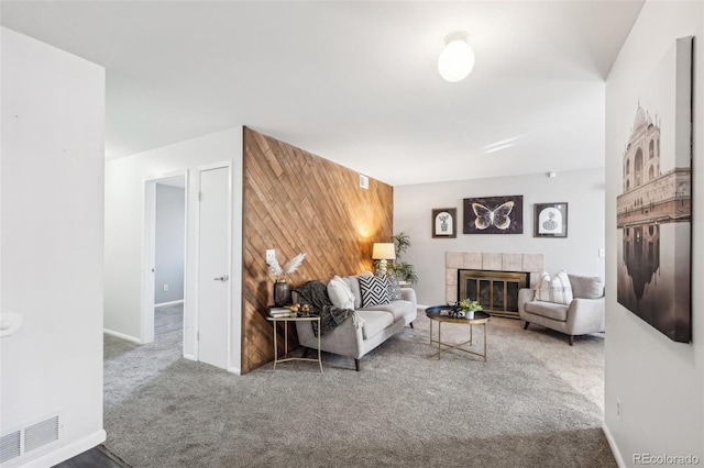 carpeted living area featuring a fireplace, visible vents, an accent wall, wood walls, and baseboards