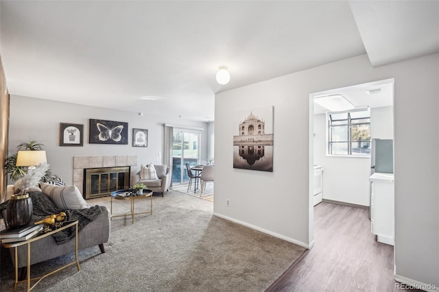 living area with baseboards, a tiled fireplace, and wood finished floors