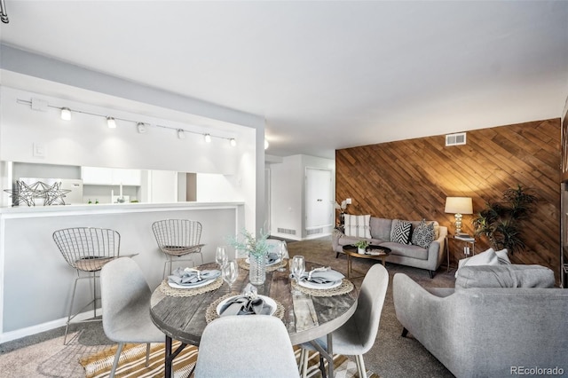 carpeted dining area with baseboards, an accent wall, visible vents, and wooden walls