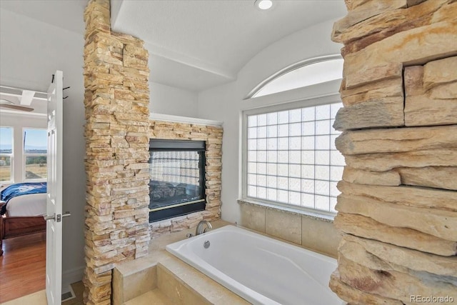 bathroom featuring hardwood / wood-style floors, plenty of natural light, and a relaxing tiled tub