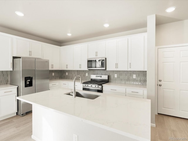 kitchen featuring appliances with stainless steel finishes, sink, white cabinets, a kitchen island with sink, and light stone countertops