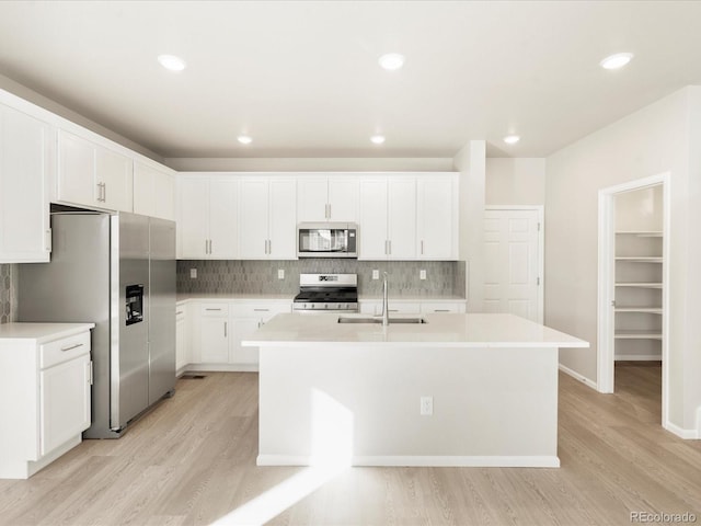 kitchen with sink, white cabinets, stainless steel appliances, a kitchen island with sink, and backsplash