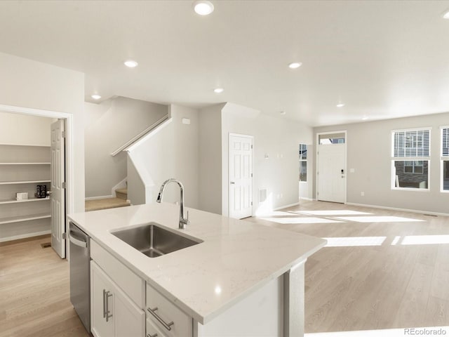 kitchen featuring dishwasher, an island with sink, sink, white cabinets, and light stone counters