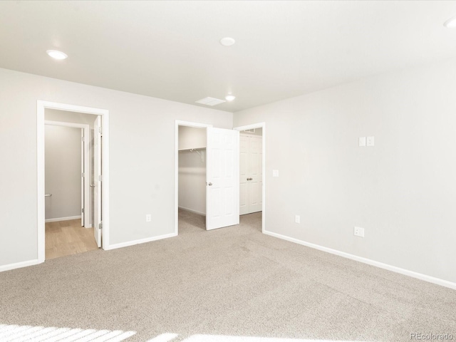 unfurnished bedroom with a walk in closet, light colored carpet, and a closet