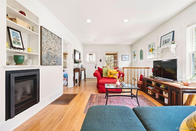 living area with recessed lighting, baseboards, a glass covered fireplace, and wood finished floors