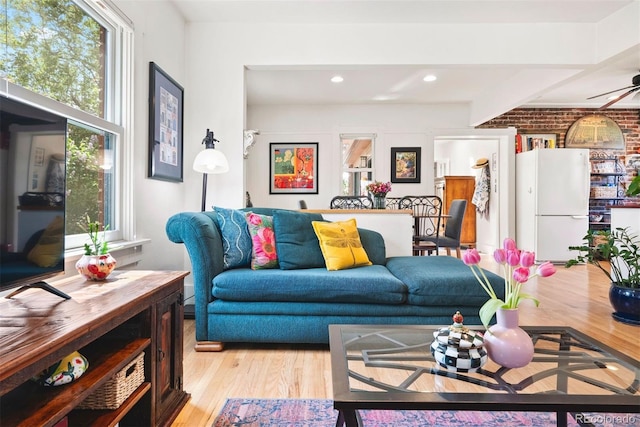 living area with a ceiling fan, brick wall, a healthy amount of sunlight, and light wood finished floors